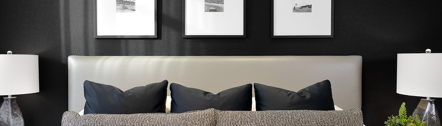 bedroom headboard with decorative pillows, black textured wall and black and white photos in frames