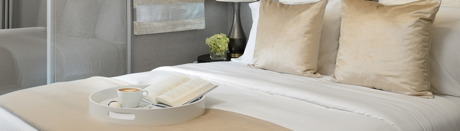 serving tray on top of a bed with an open book and latte
